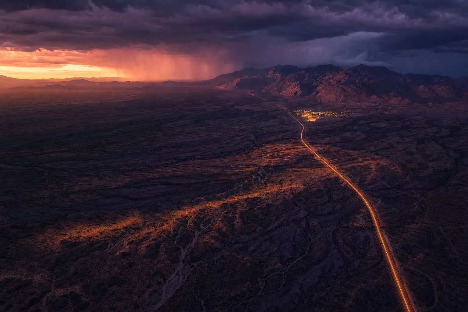 Aerial view of the Sonoran Desert at dusk, monsoon cloud stacked over lit highways and a distant resort complex